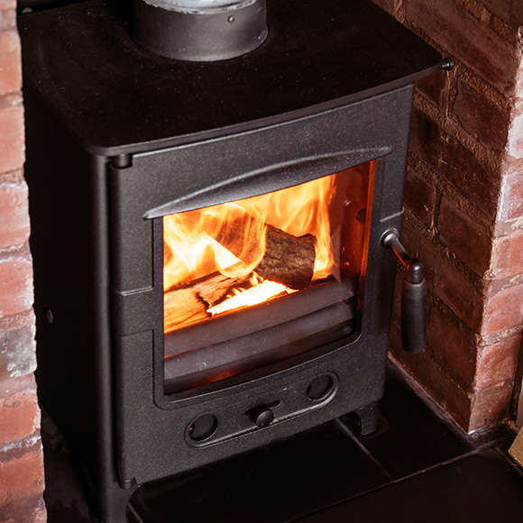 a log burner in a brick nook with wood burning within