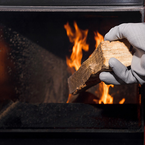 a grey gloved hand placing firewood into a log burner